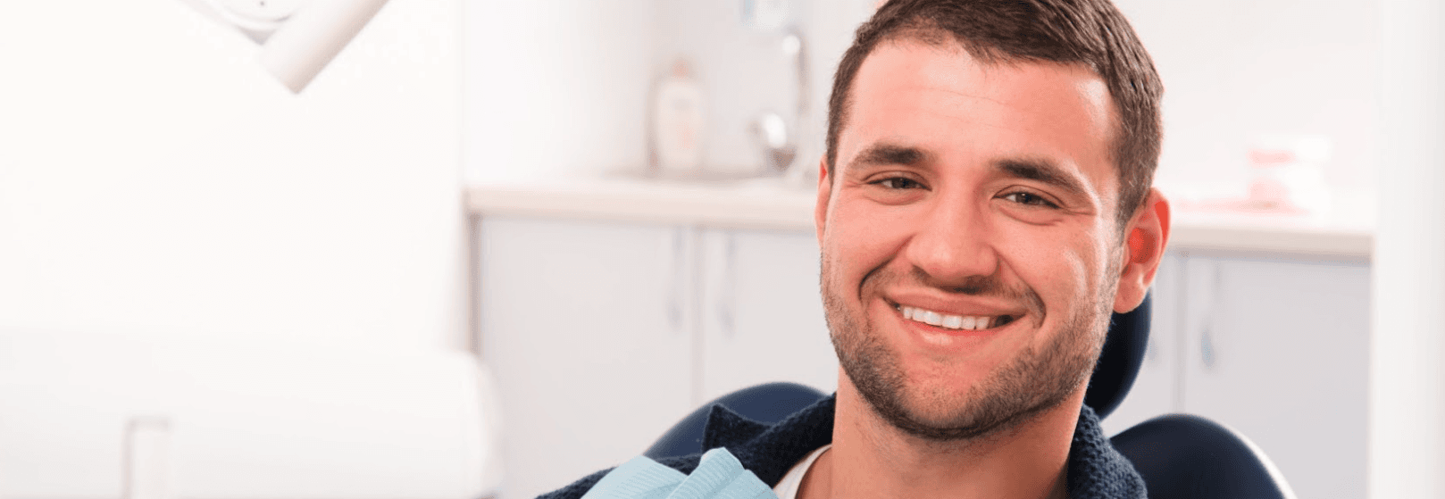 A man sitting on a dentist chair, with his mouth open and his teeth visible